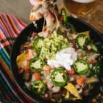 hand pulling a single brisket nacho from the cast iron skillet