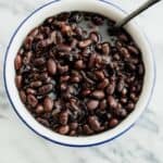 homemade Mexican style black beans in a white bowl with a blue rim