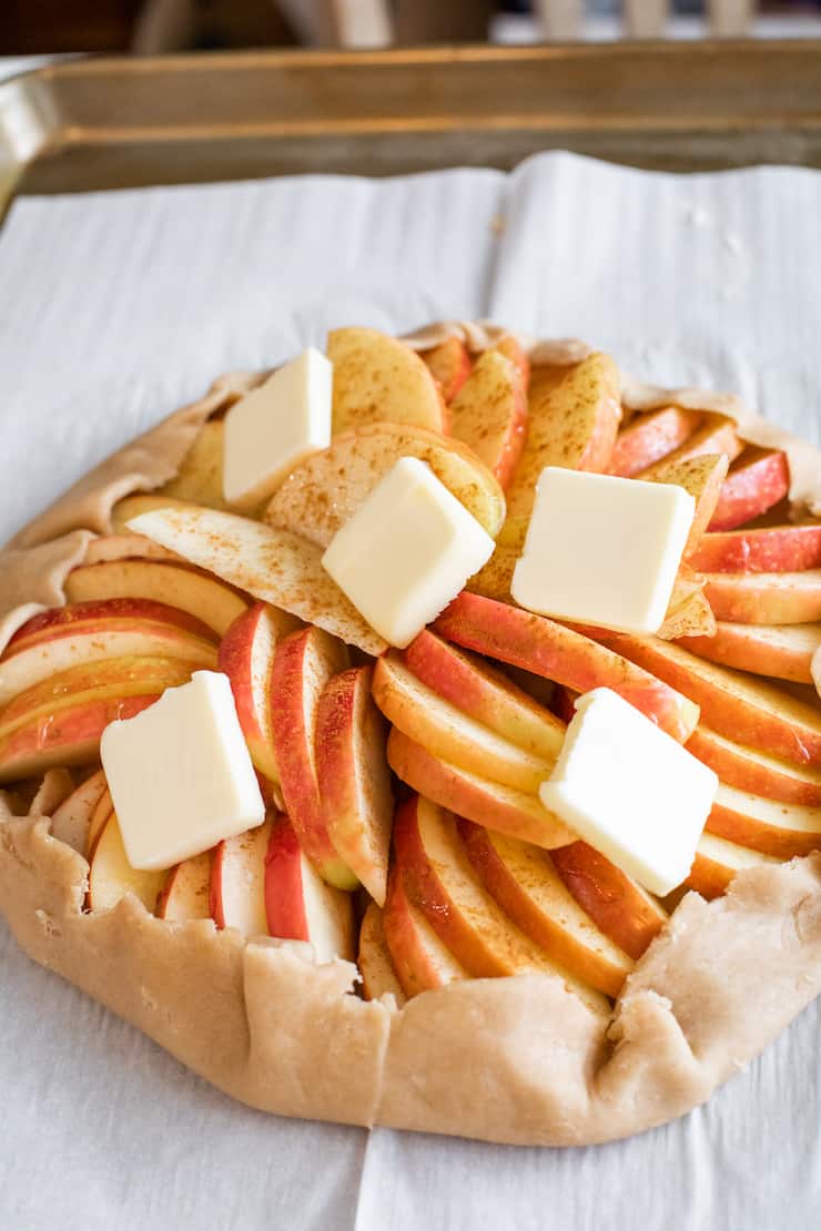 Unbaked rustic apple galette with folded crust and pats of butter on top, ready to bake.