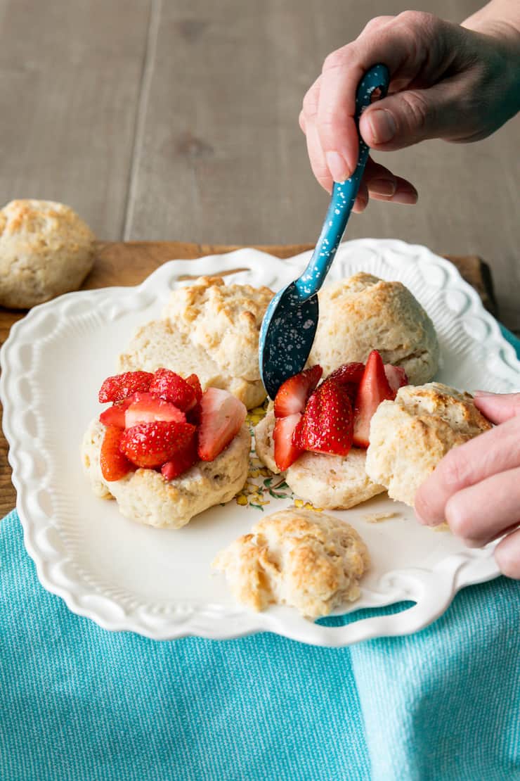 hands assembling homemade strawberry shortcakes out of easy drop biscuits on a white platter