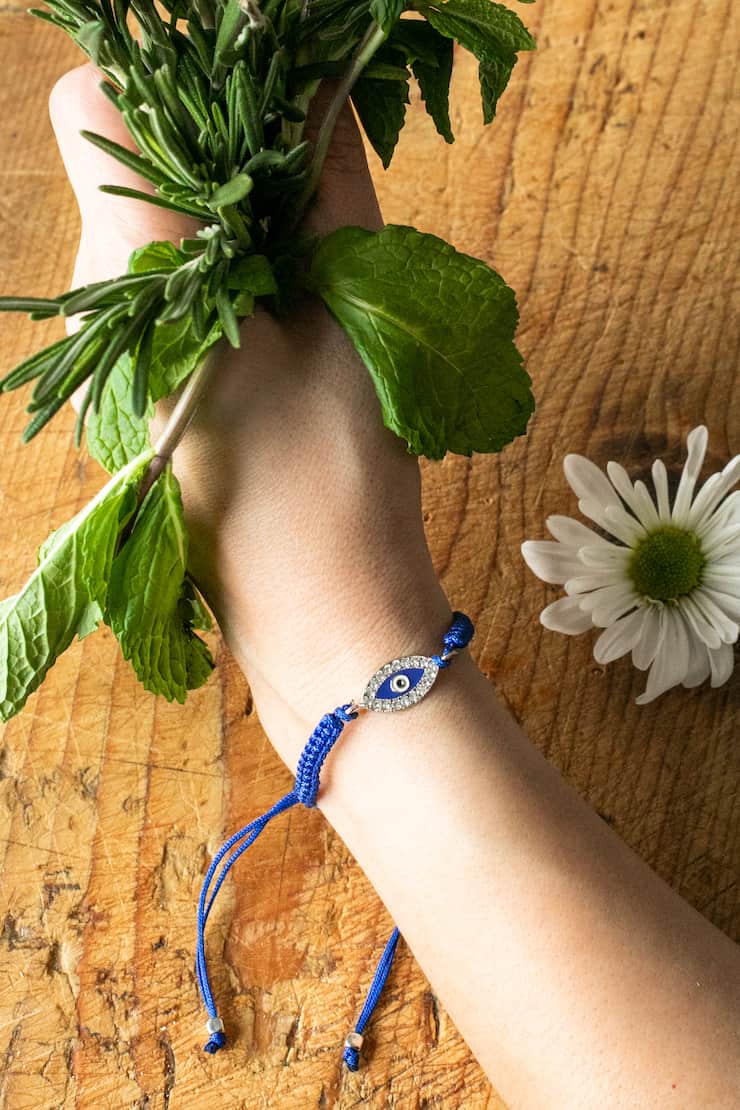 hand holding a bouquet of fresh herbs and wearing an evil eye bracelet 