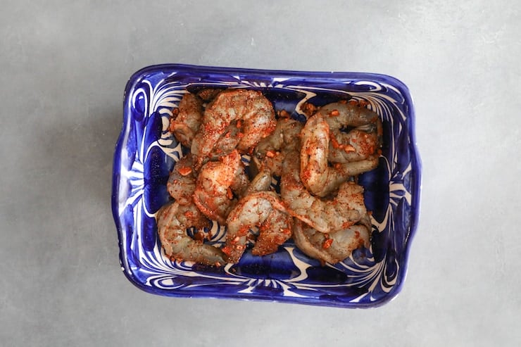 raw shrimp tossed in paprika garlic spice mix in blue and white bowl