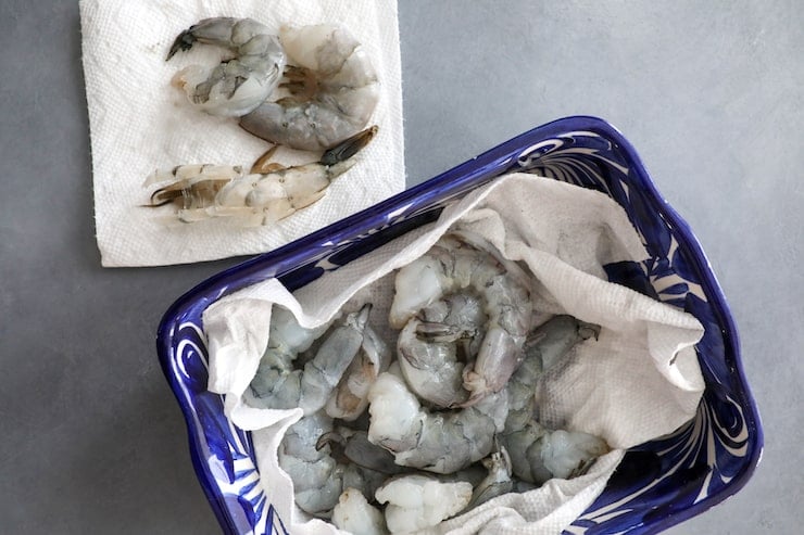 raw shrimp in a blue bowl with paper towels to dry