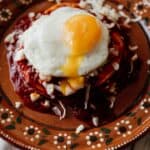 stacked red enchiladas on an earthenware plate with a fried egg on top
