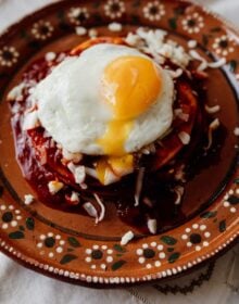 stacked red enchiladas on an earthenware plate with a fried egg on top