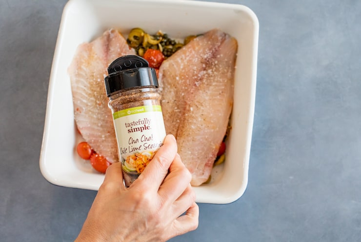 hand shaking "tastefully simple" cha cha chile lime seasoning blend over fish