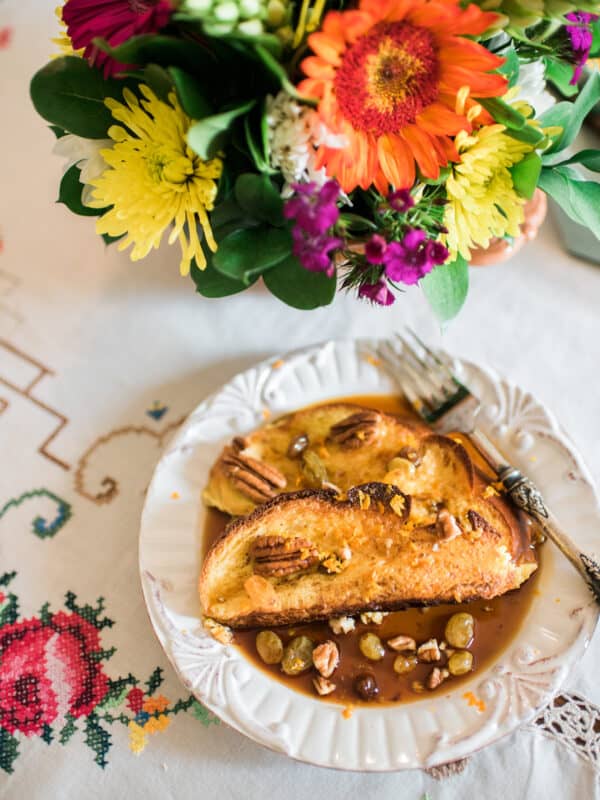Two slices of Baked Mexican French Toast Torrejas on a white plate served with flowers on the side