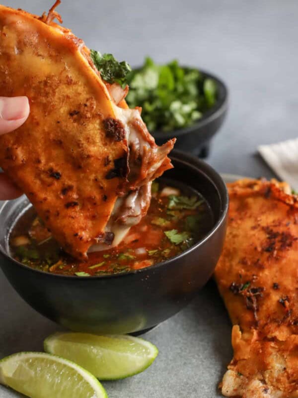 Crispy birria tacos dipped in rich birria consommé with cilantro, onion, and lime, from the authentic Birria de Res recipe by Yvette Marquez of Muy Bueno.