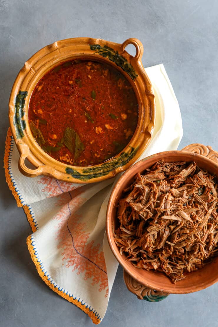 flat lay shot of shredded birria de res next to an earthenware bowl of birria consomme. 