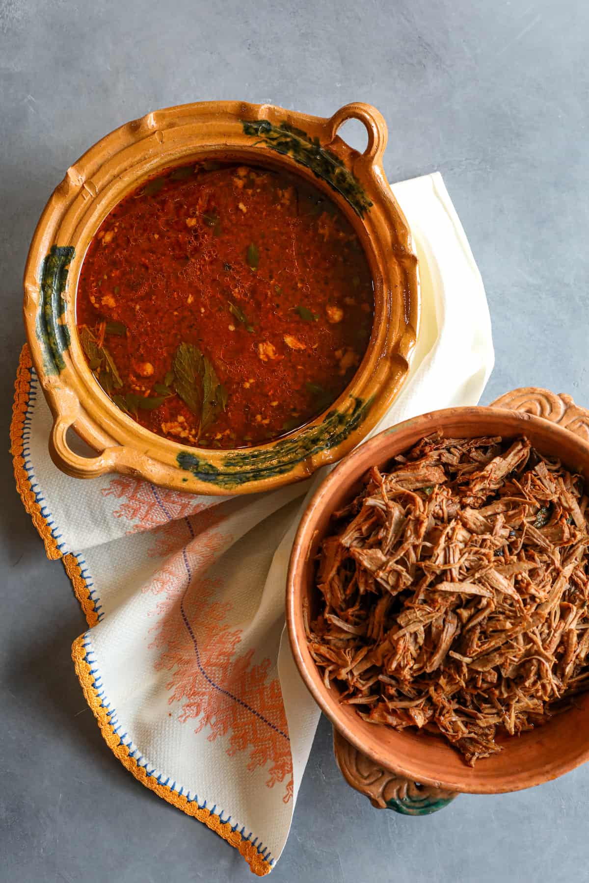 overhead shot of shredded birria de res in a terracotta bowl with a separate bowl filled with the birria broth