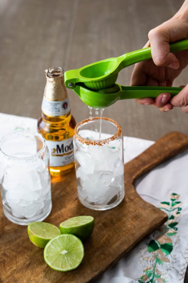 hand squeezing lime juice into a glass of ice that has been rimmed with tajin seasoning