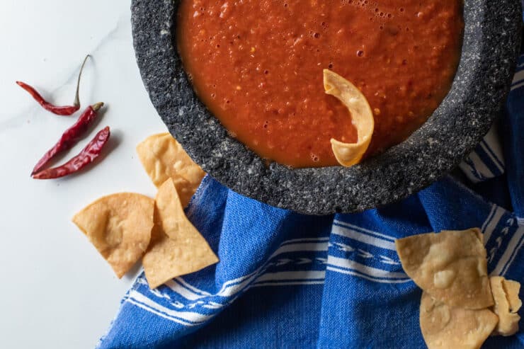 overhead shot of a bowl of chile de arbol spicy salsa with a blue and white tea towel and crispy tortilla chips