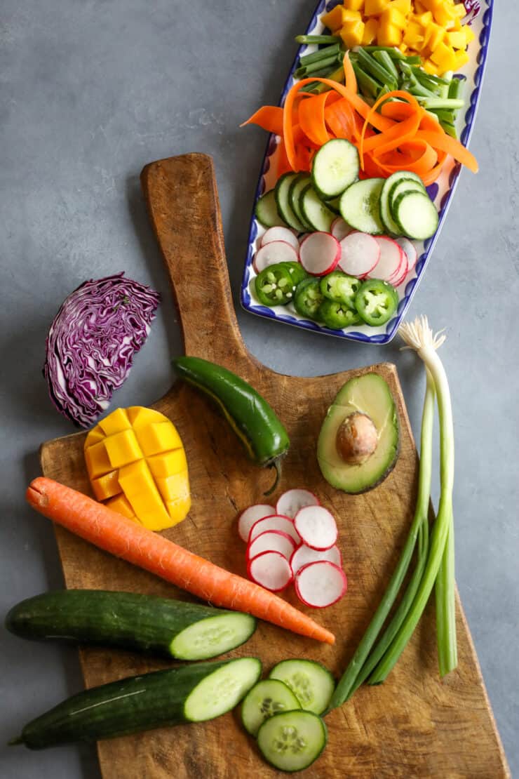 wooden cutting board with avocado, mango, green onion, cucumber, jalapeño and cabbage for poke bowls