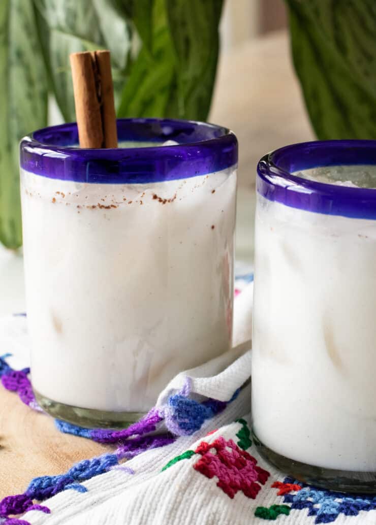 two blue-rimmed glasses filled with homemade horchata and garnished with cinnamon sticks