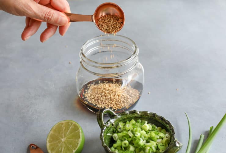 hand pouring sesame seeds into a jar with other tuna poke marinade ingredients