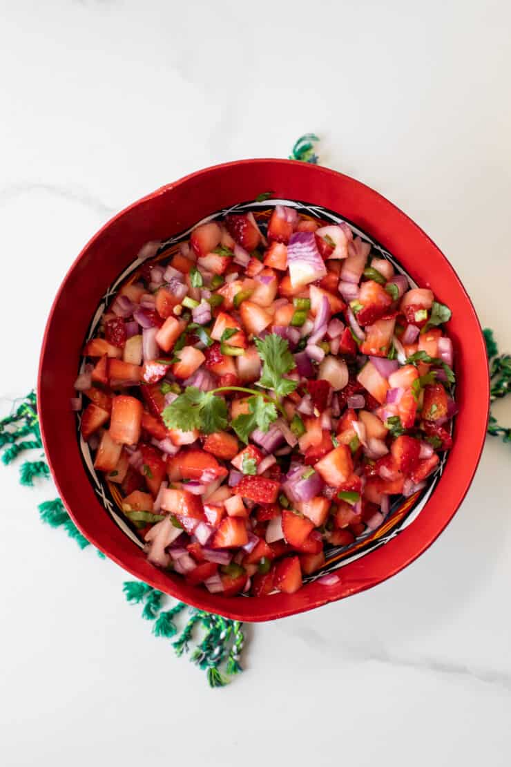 overhead shot of strawberry pico de gallo style salsa in a red bowl on a white table