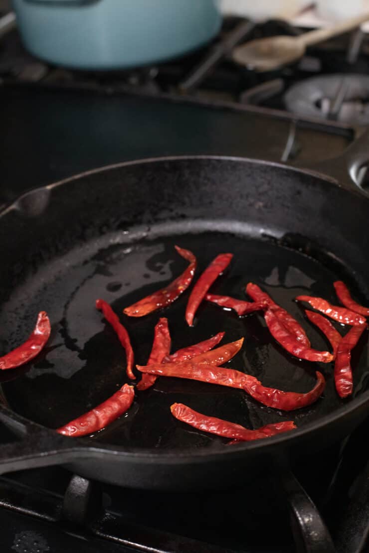 chiles de arbol frying in a cast iron skillet