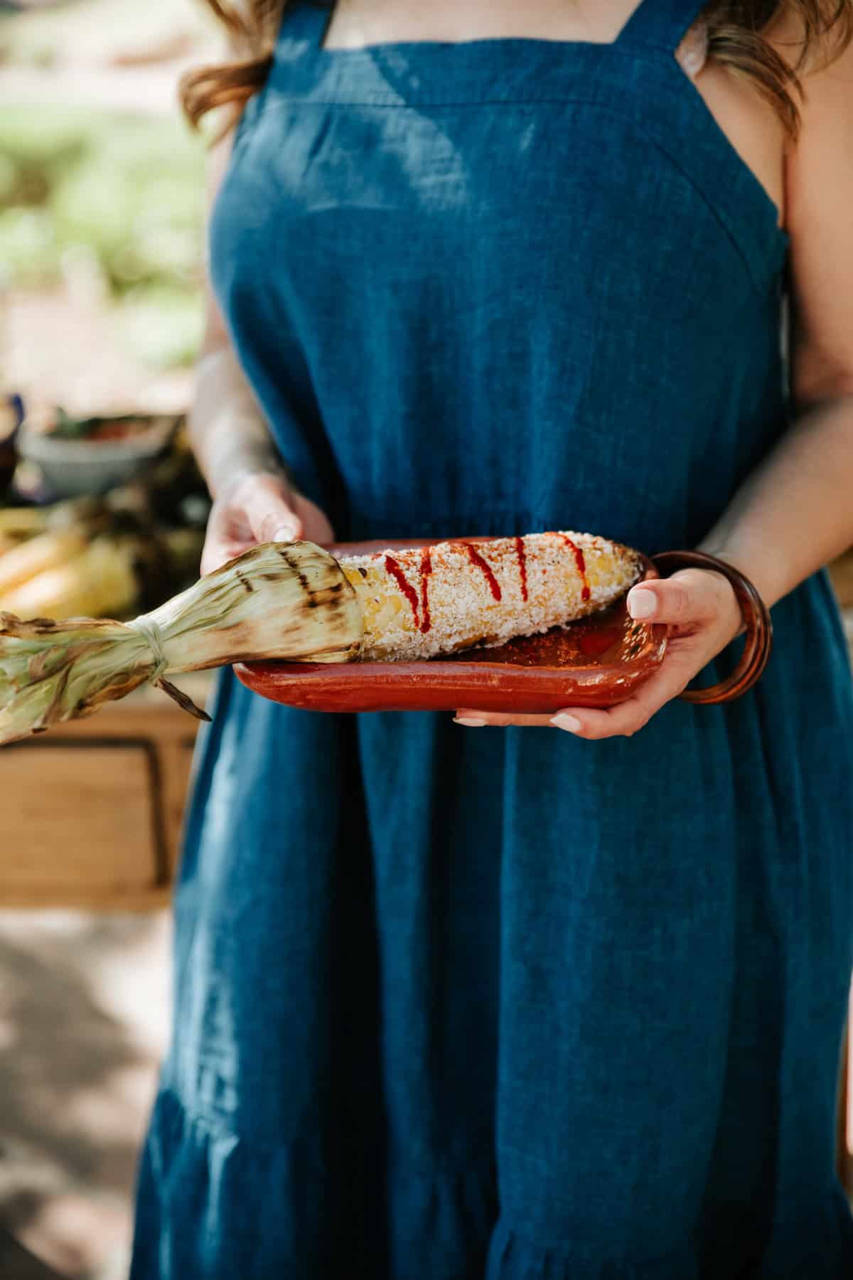 Homemade Mexican street corn (elote) served on a clay platter, topped with Mexican crema, cotija cheese, chile powder, and hot sauce.