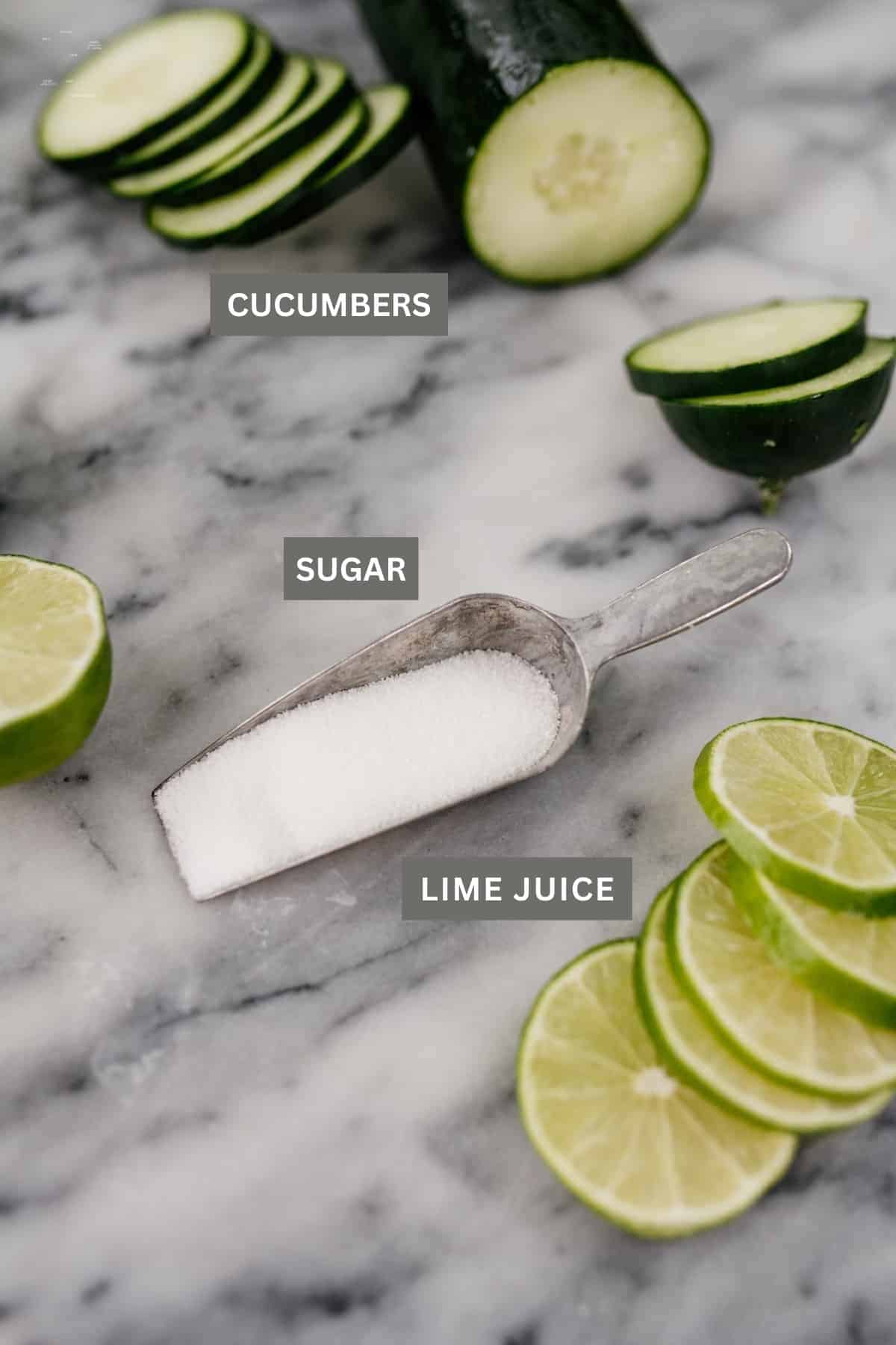 Slices of cucumber, limes, and a scoop of sugar on marble board.