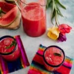 pitcher of agua de sandia with two cups filled with the watermelon agua fresca and garnished with mint.