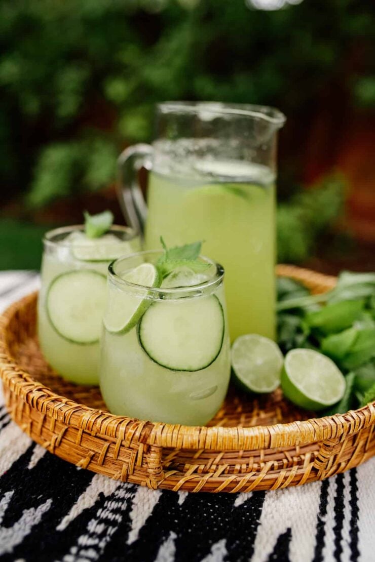 two glasses and a pitcher of cucumber agua fresca garnished with lime and mint