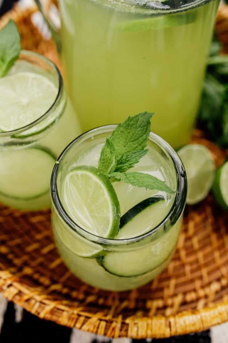 two glasses of agua de pepino garnished with mint and lime on a rattan serving tray