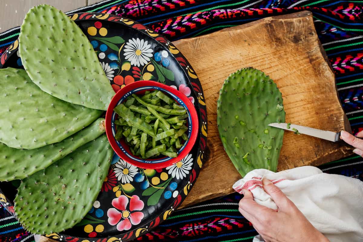 process shot - showing how to prep by removing spines, using a towel to protect your hands. The nopales to the left are both whole and diced on a Colorado platter on a cutting board. 