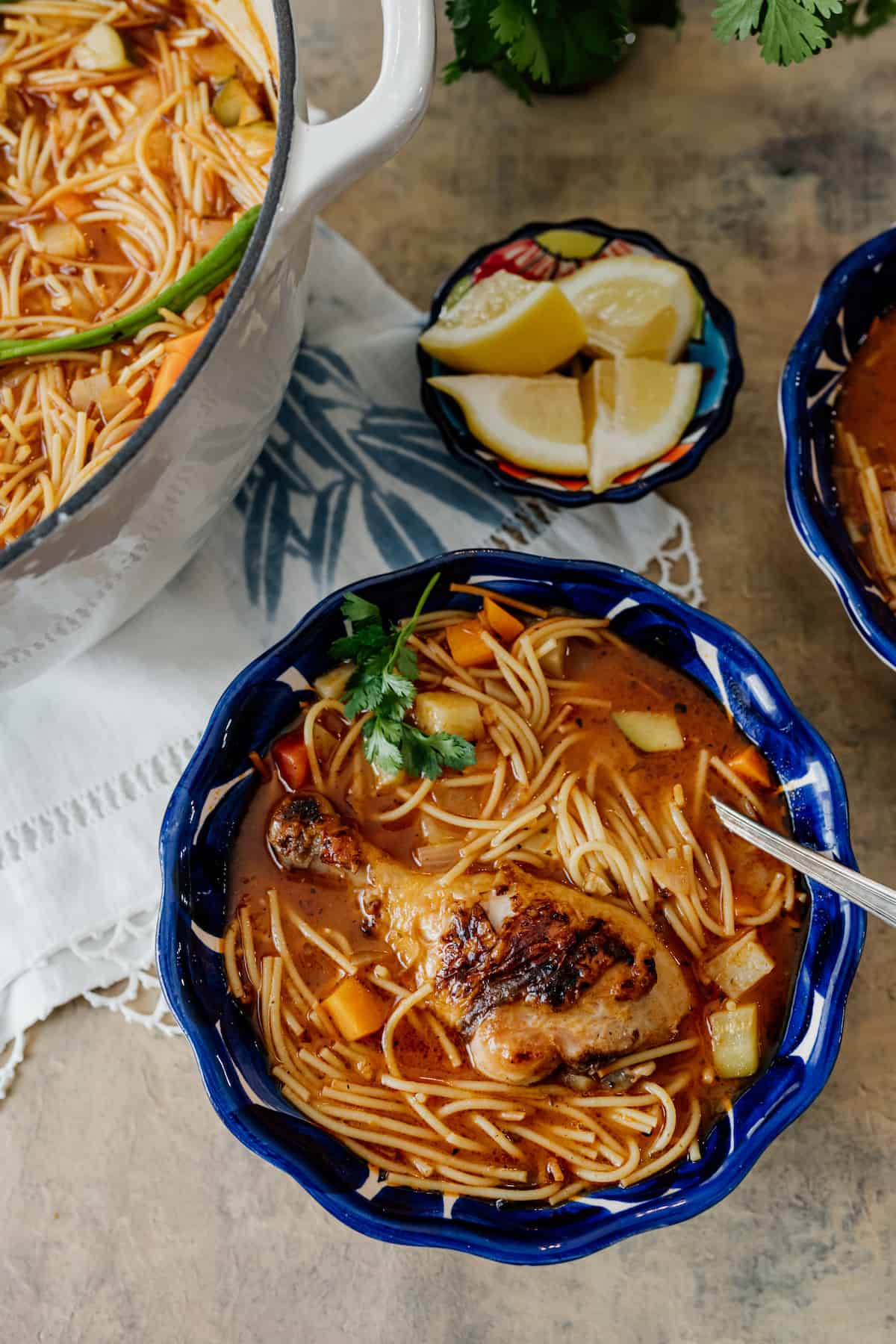 Sopa de Fideos con Pollo, a Mexican version of chicken noodle soup in a Mexican blue bowl with a side of lemons