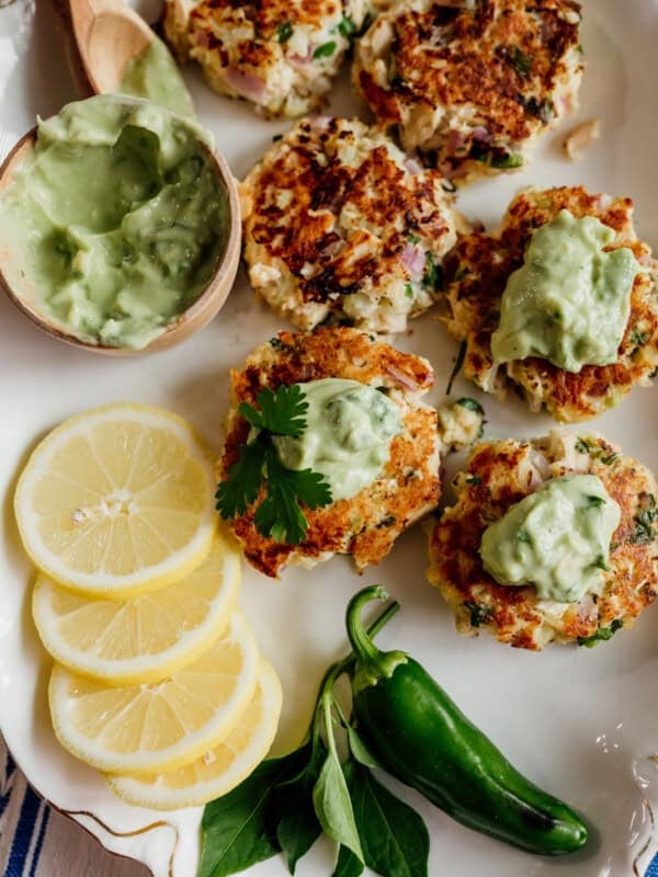 tuna patties with avocado Crema on a vintage white platter with lemon slices and jalapeño on the side.