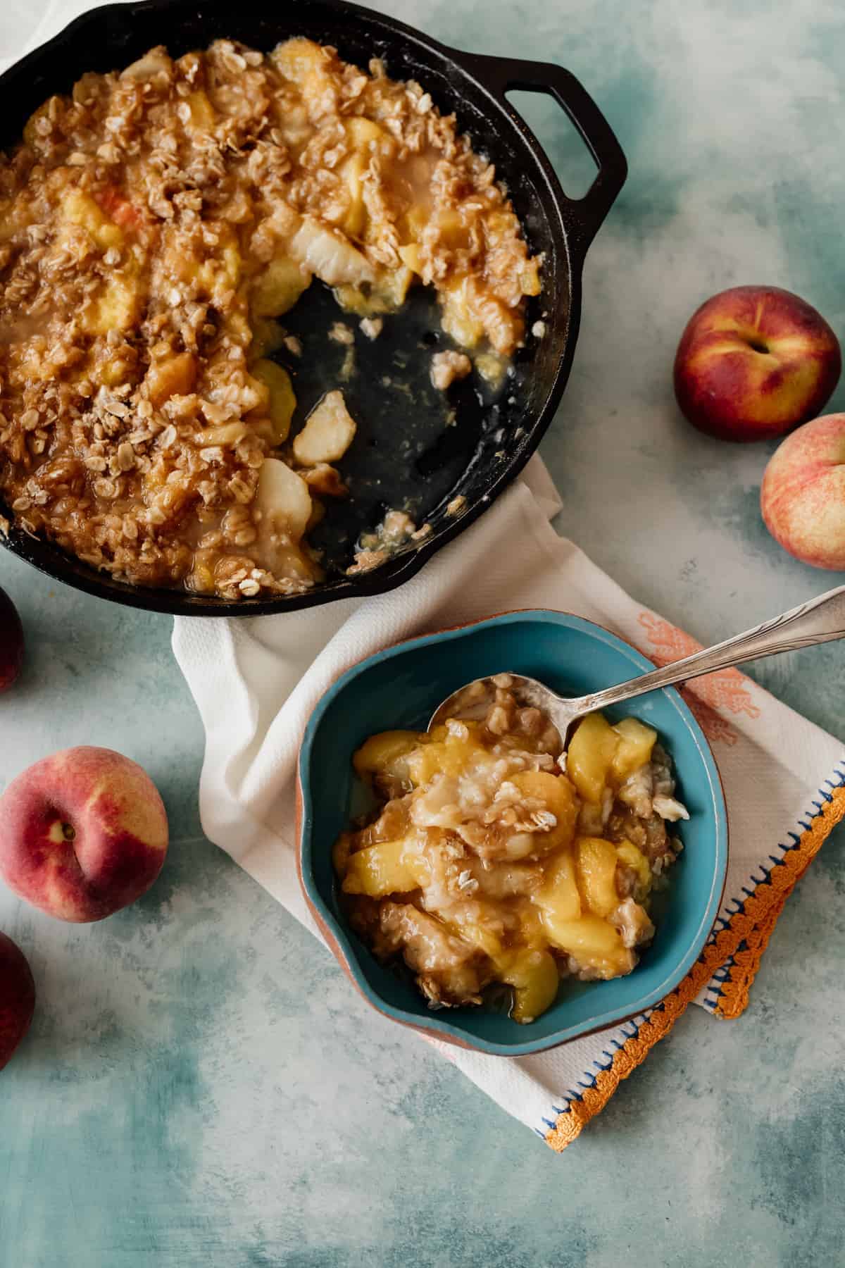 overhead shot of peach crisp made in a cast-iron skillet with a blue bowl filled with some of the crisp. 