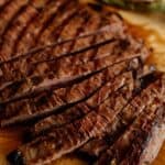 Grilled carne asada sliced against the grain on a cutting board, showcasing juicy, tender steak with charred grill marks.