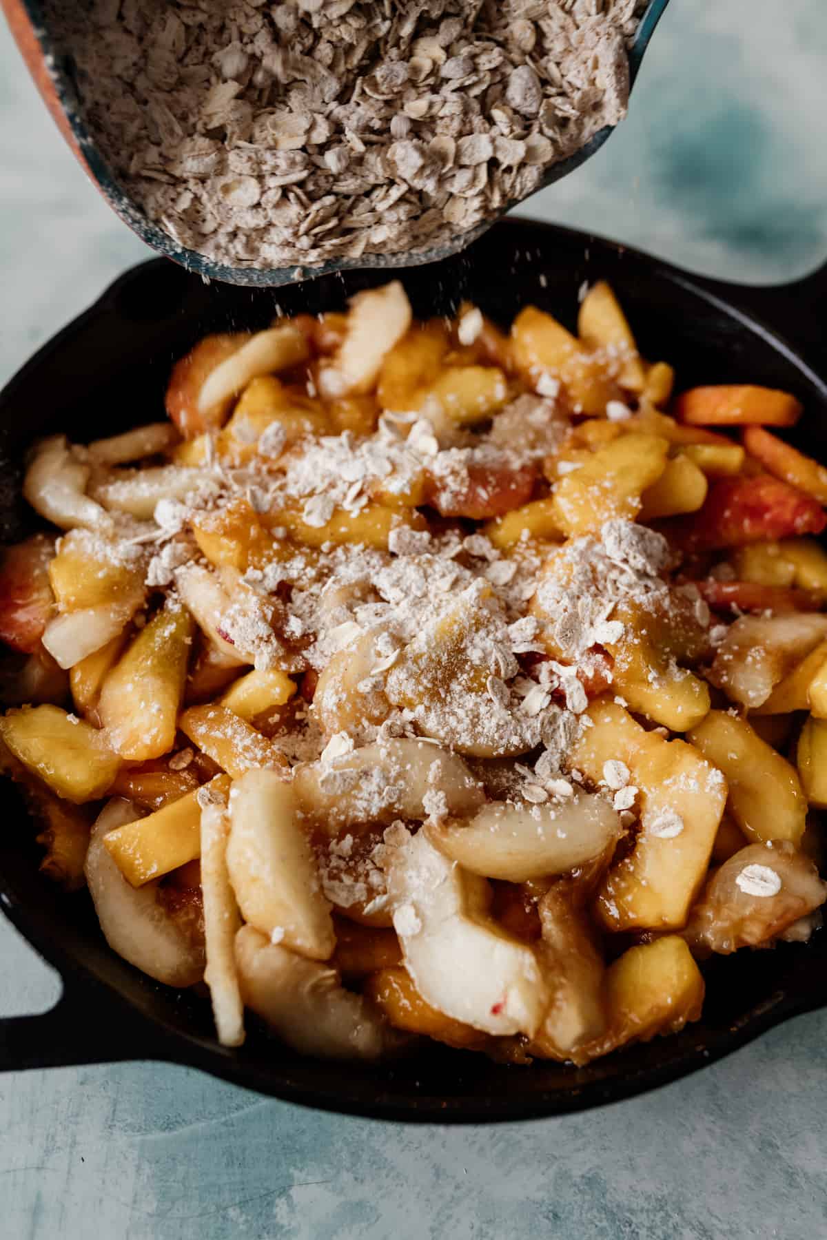 sprinkling oats over sliced peaches in a cast iron skillet for a peach crisp.