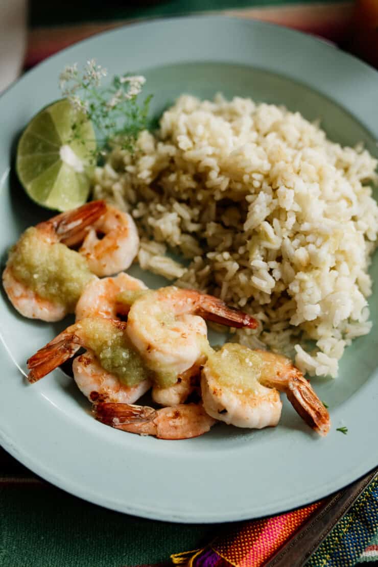 shrimp served with Mexican green rice and drizzled with bright and flavorful salsa verde on a teal enamel plate with a lime wedge 