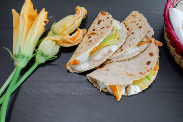 squash blossom quesadillas on a black slate board with squash blossoms on the side