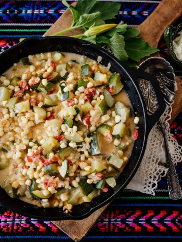 Calabacitas con Elote (Zucchini with Corn) topped with cheese on a board and colorful striped fabric