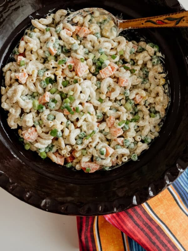 Ensalada de Coditos (Macaroni Salad) in a Mexican brown barro bowl with wooden spoon and striped napkin.