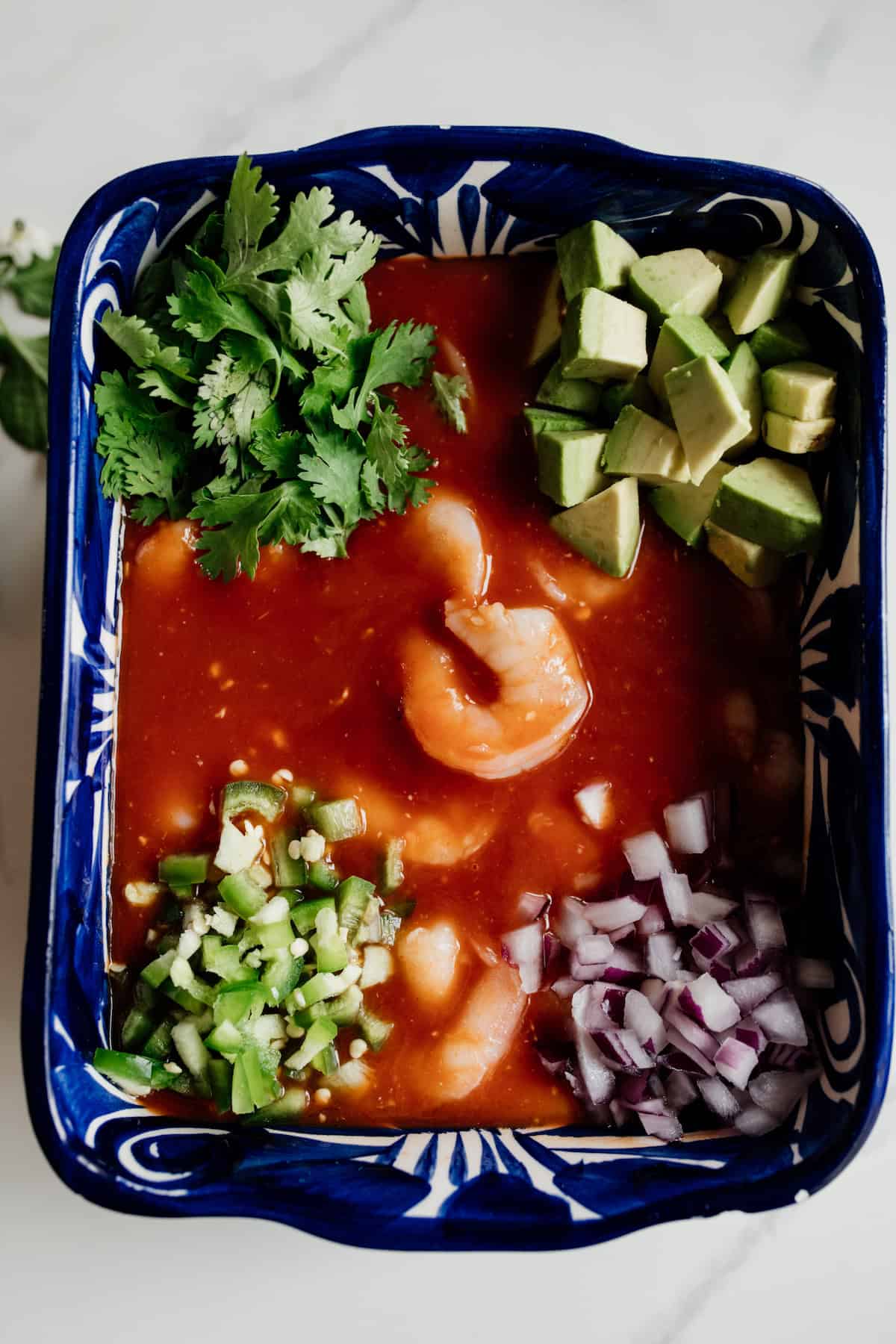 all ingredients for making Mexican coctel de camarones added to a rectangular blue serving dish before stirring it together.