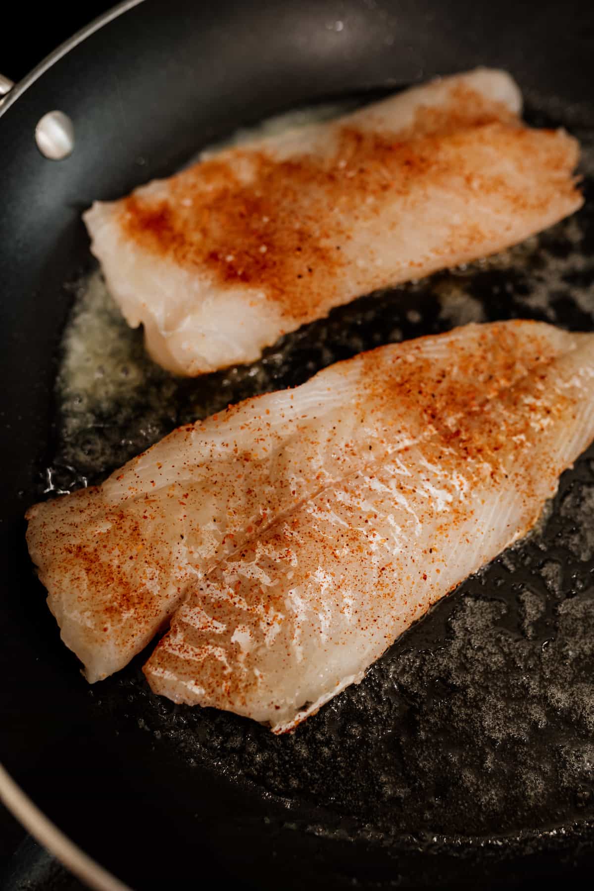 cod fish being cooked on a skillet with butter.