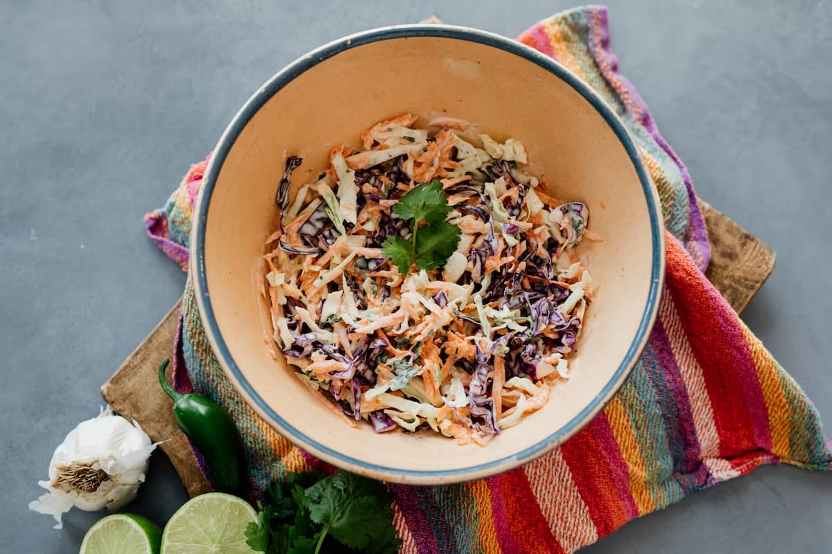 homemade fish taco coleslaw in a beige bowl under a colorful striped napkin .