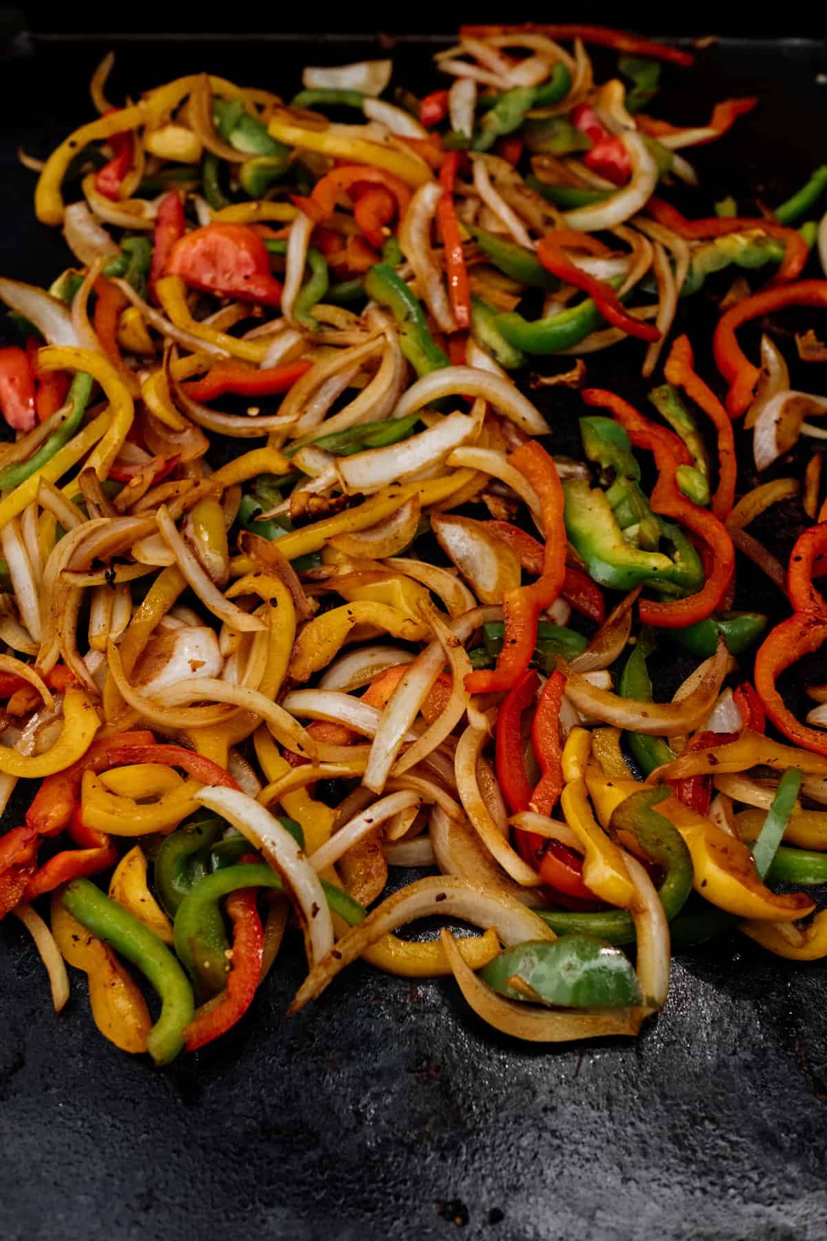 cooked colorful bell peppers and onions on a griddle