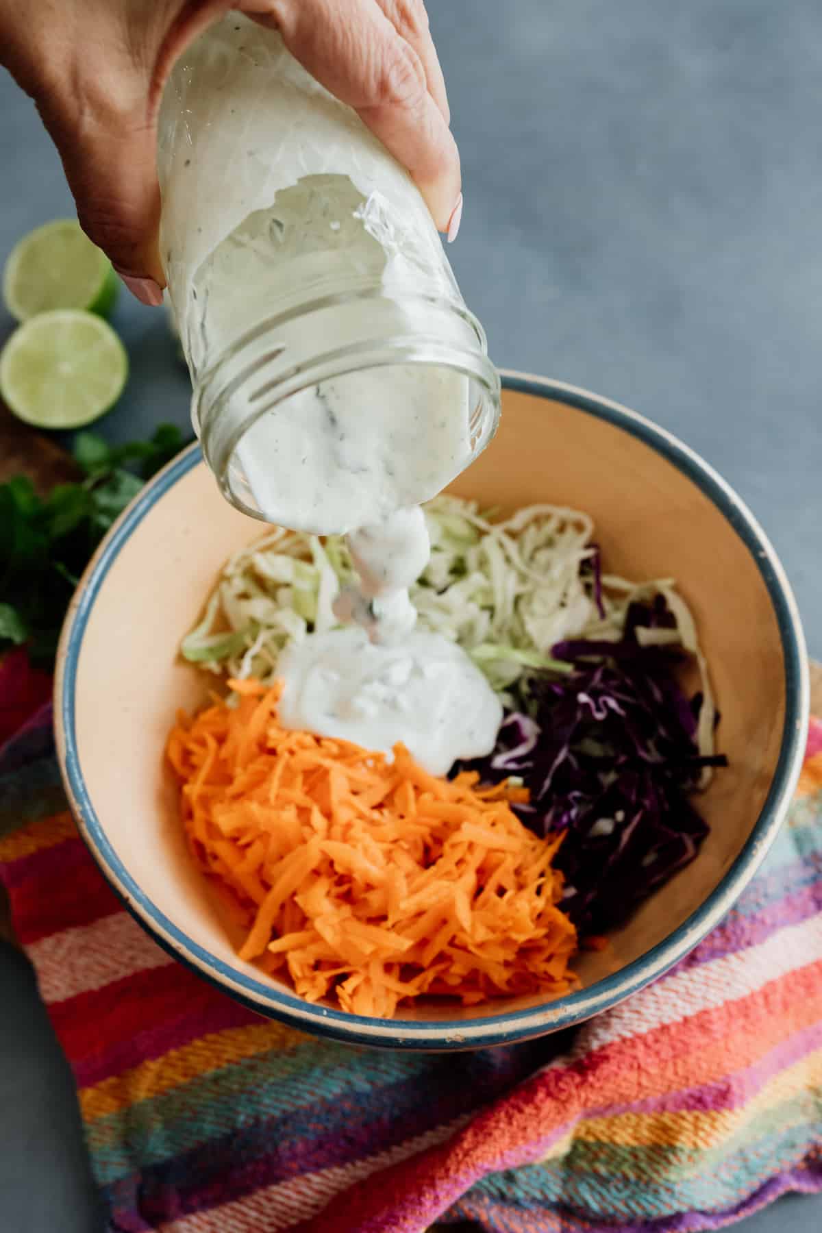 hand holding a mason jar and pouring dressing in a bowl of cabbage and shredded carrot to make a creamy fish taco slaw.