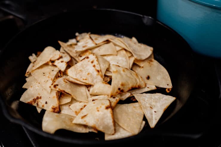 homemade pan-fried tortilla chips in a cast iron pan for making green chilaquiles.