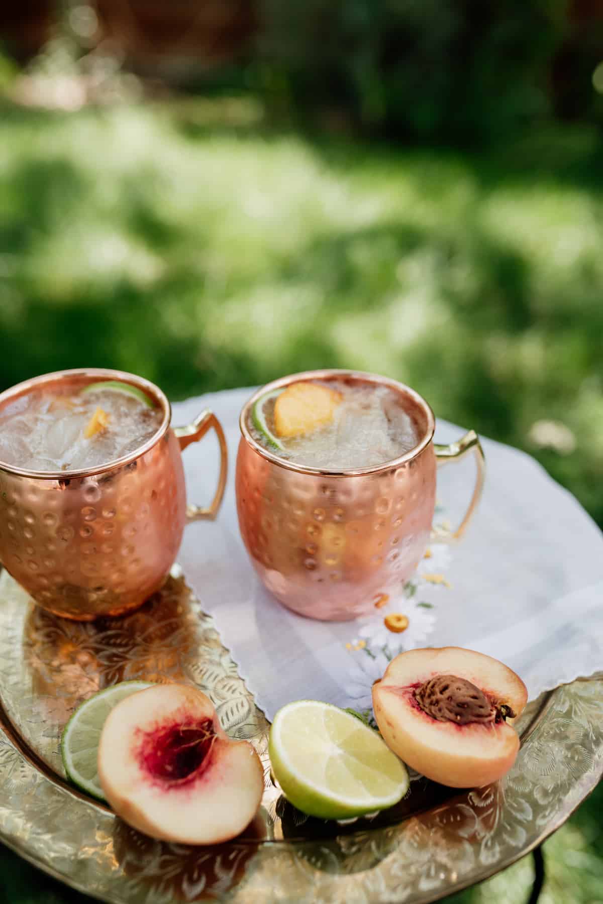two copper mugs filled with peach kentucky mule on a silver platter