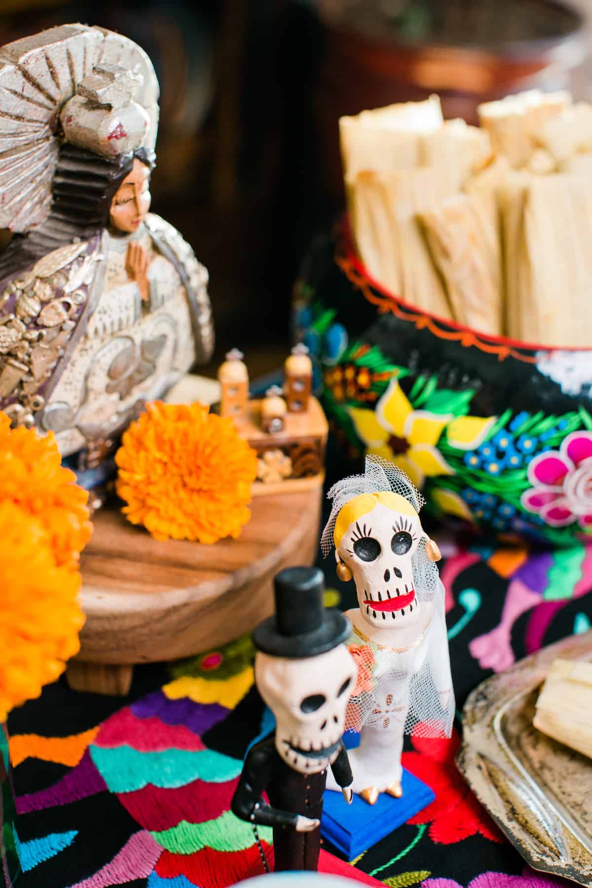 a mini alter for Dia de los Muertos adorned with candles, marigolds, figurines, and pumpkin spice tamales