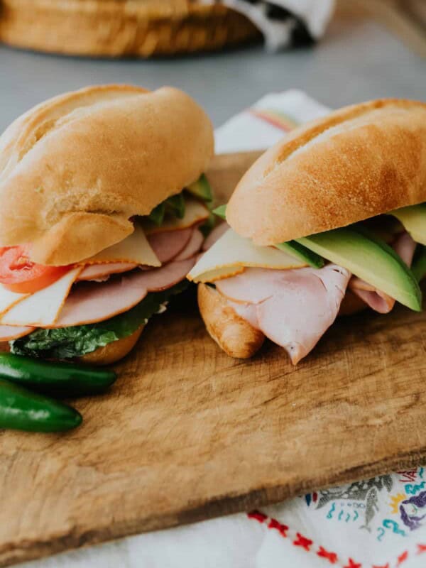 Two Mexican tortas on a cutting board with jalapenos on the side.