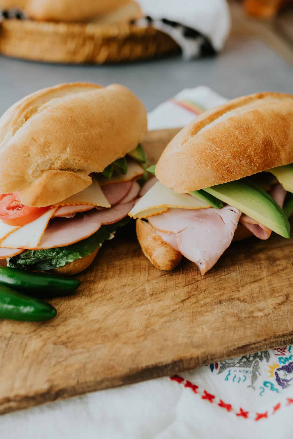 two tortas de jamon on a wooden cutting board with two whole jalapeños