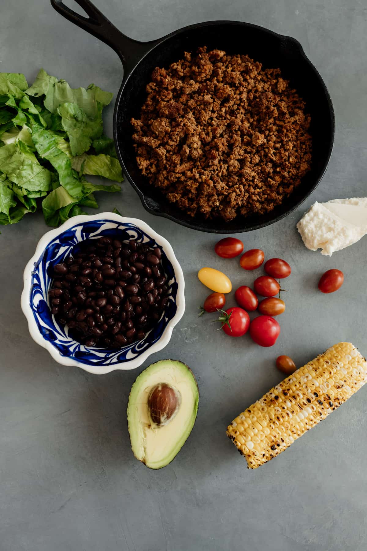 skillet with ground bison and ingredients for a taco salad - corn, avocado, tomatoes, black beans