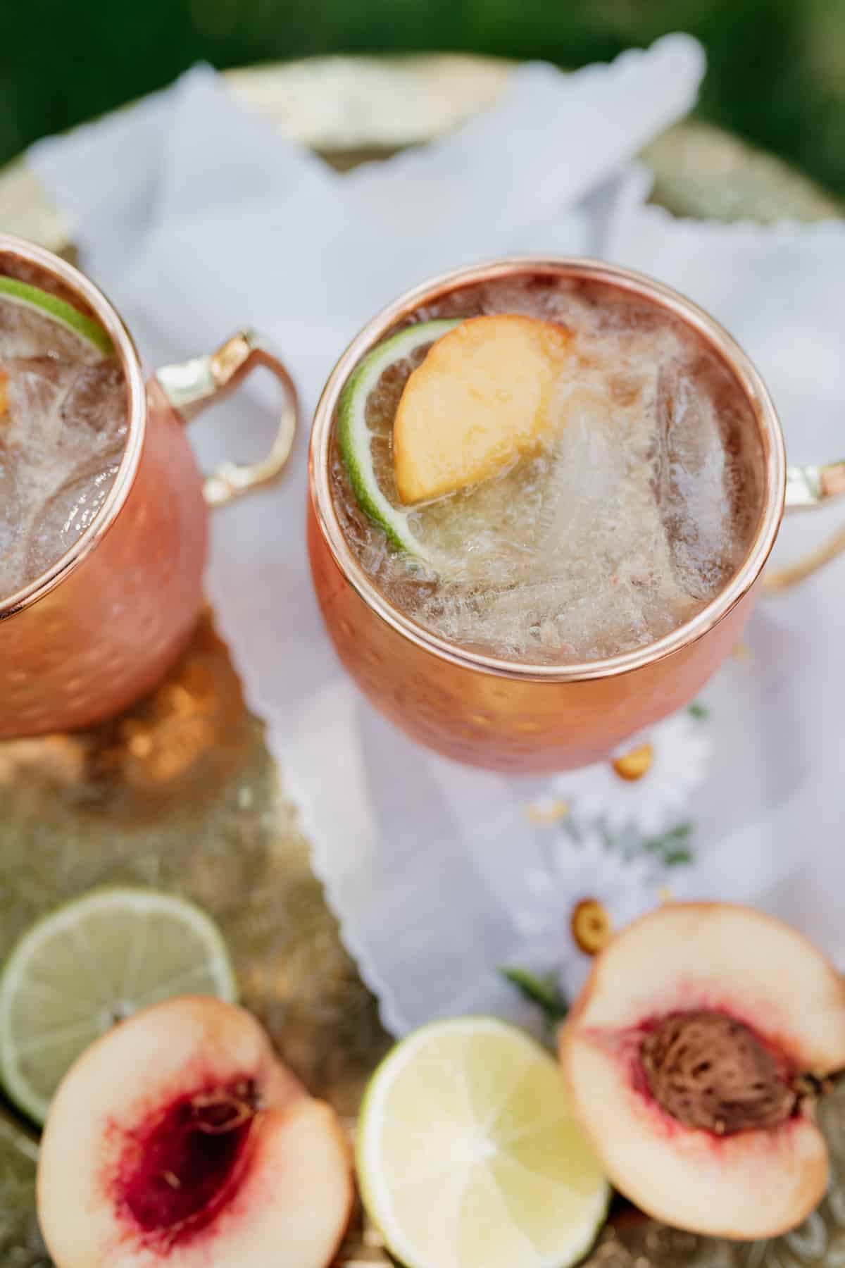 overhead shot of two copper mugs of peach kentucky mules on an embroidered napkin