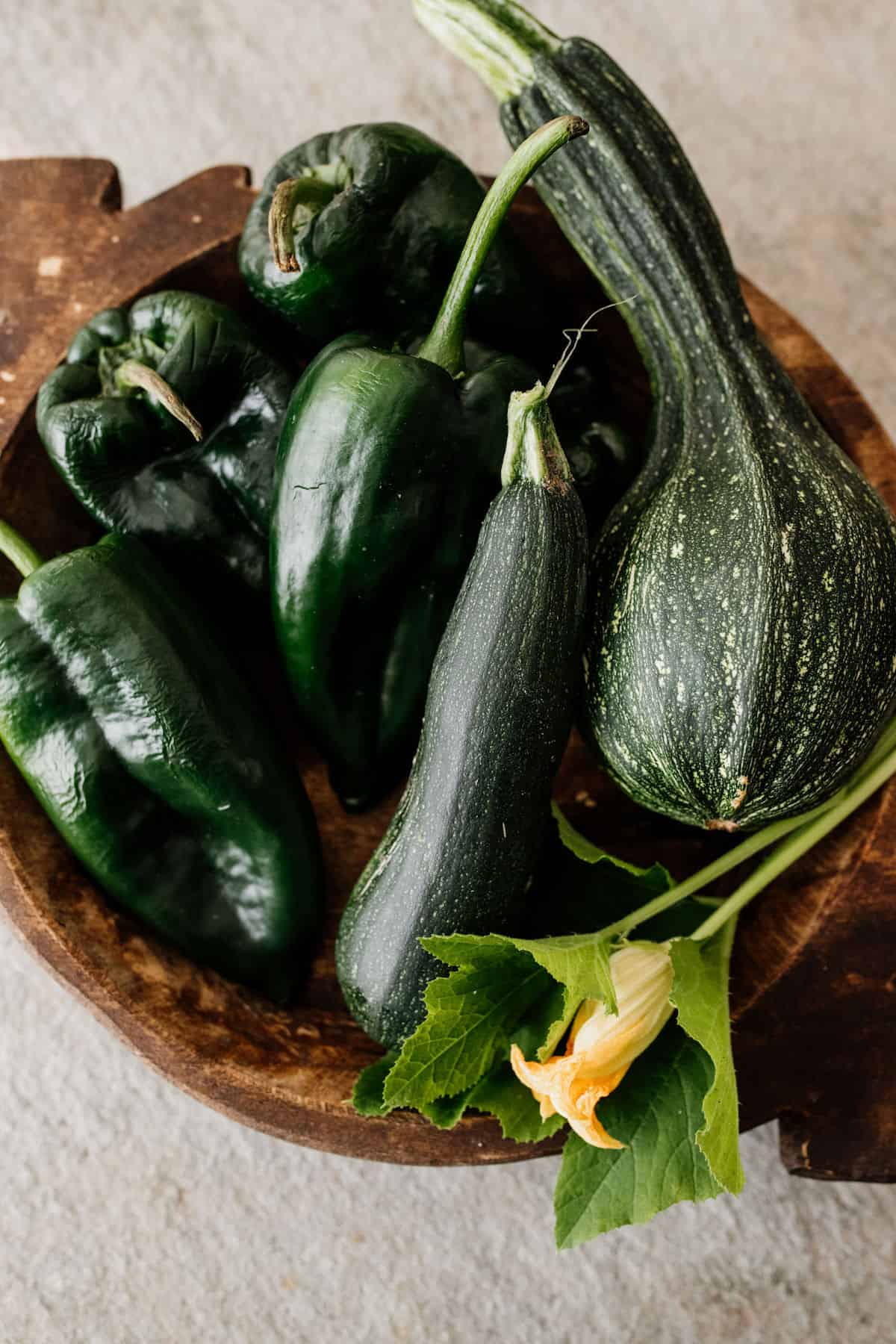 a brown wooden bowl filled with zucchini and poblanos from the garden 