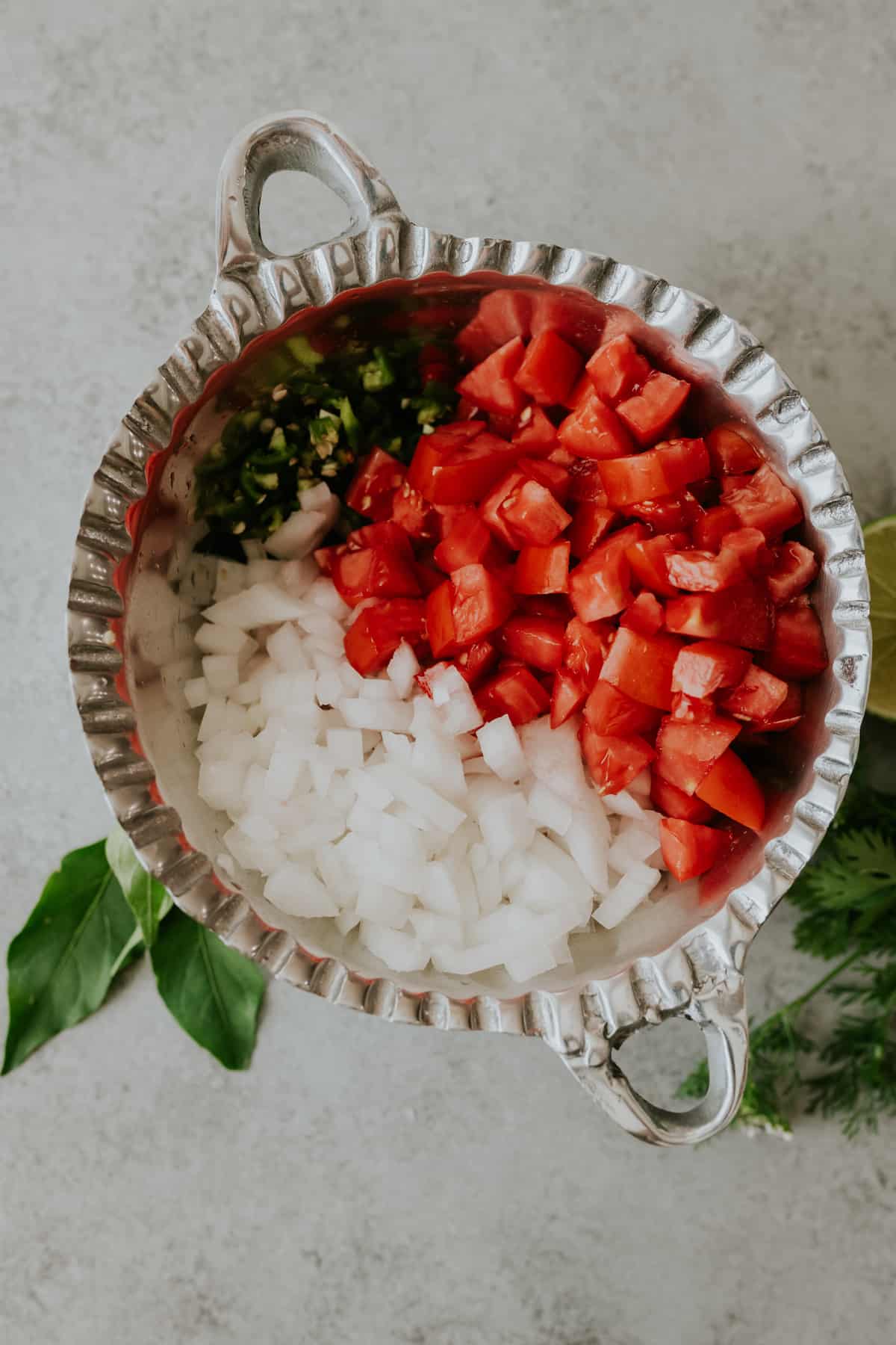 Chopped salsa bandera ingredients arranged in a large silver serving bowl with two handles